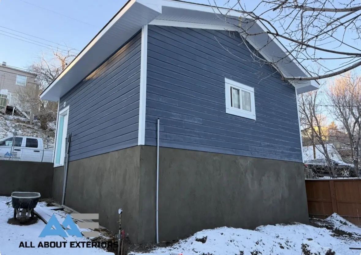 Side of a detached garage finished in blue Hardie lap siding with white trim over a grey parged base