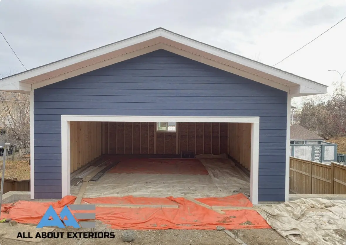 Front of a double garage in blue Hardie siding with white trim around the door opening