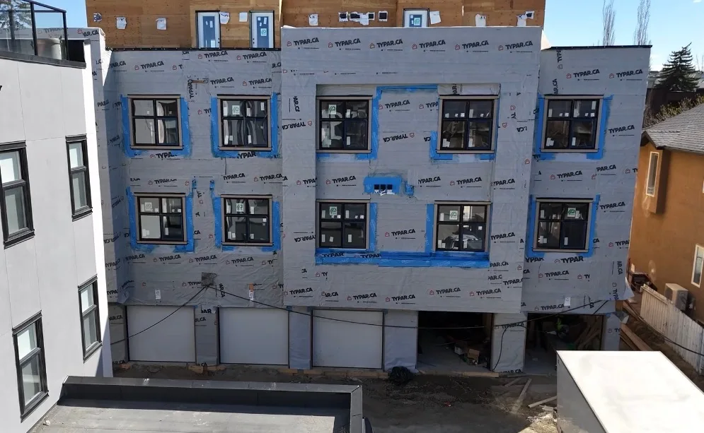 Three storey building wrapped in Typar house wrap with blue membrane around the new black windows