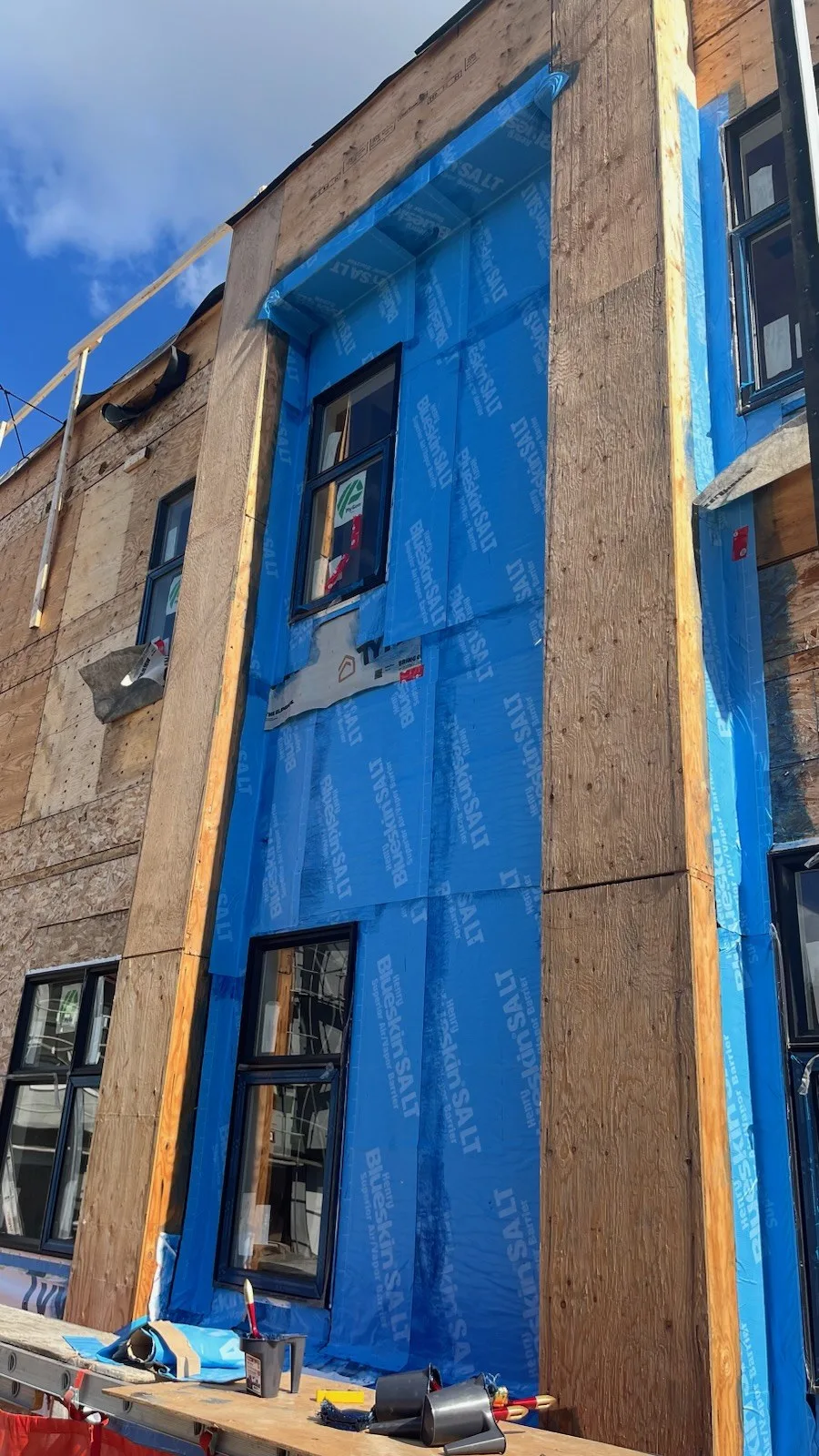 Blue weather barrier membrane wrapped around the windows on a wood sheathed wall