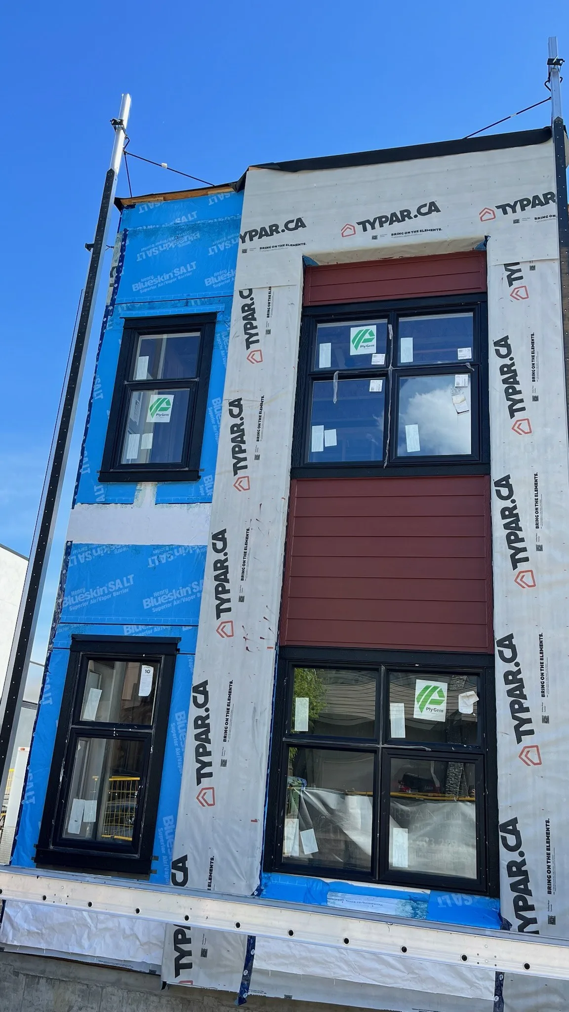 Three storey infill wrapped in Typar house wrap with blue membrane and new black windows