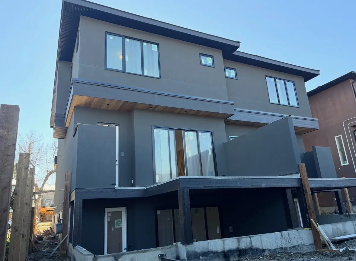 Rear of a three storey stucco home with black windows, cedar soffit and covered decks