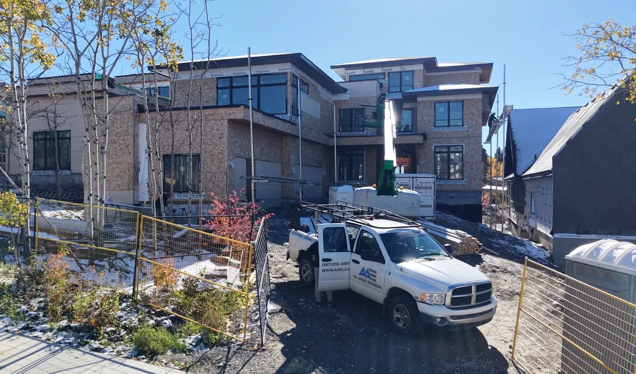 Large custom home framed and wrapped in Tyvek with an All About Exteriors truck and boom lift out front