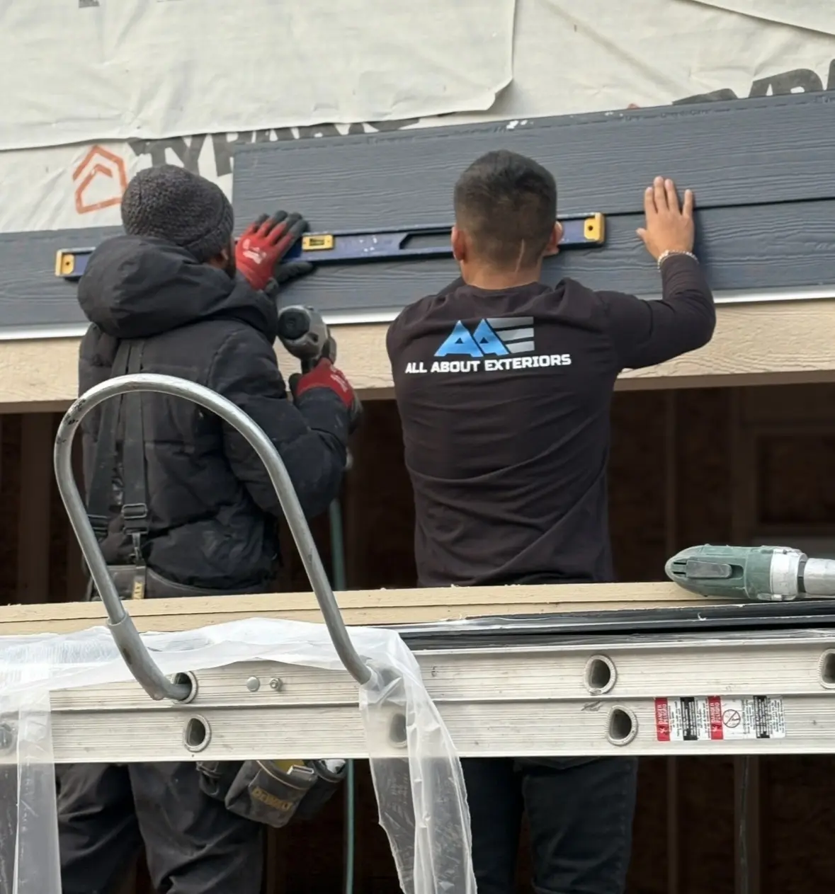 Two All About Exteriors installers leveling a James Hardie panel over house wrap