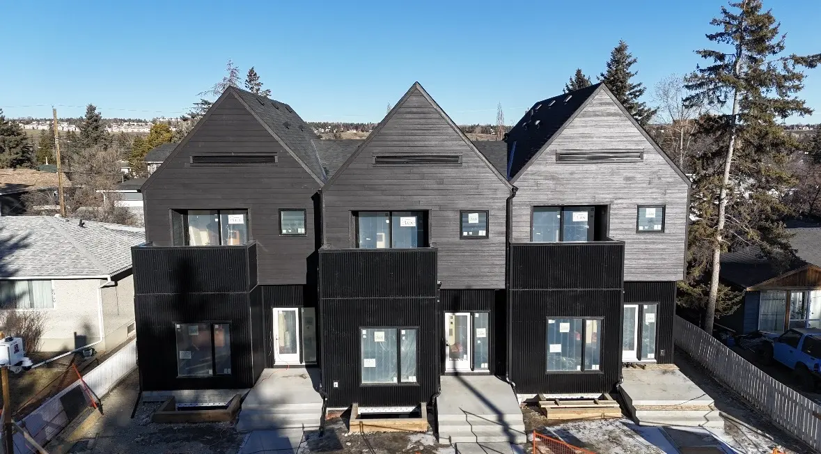 Row of three modern townhomes clad in dark vertical siding with black panel accents
