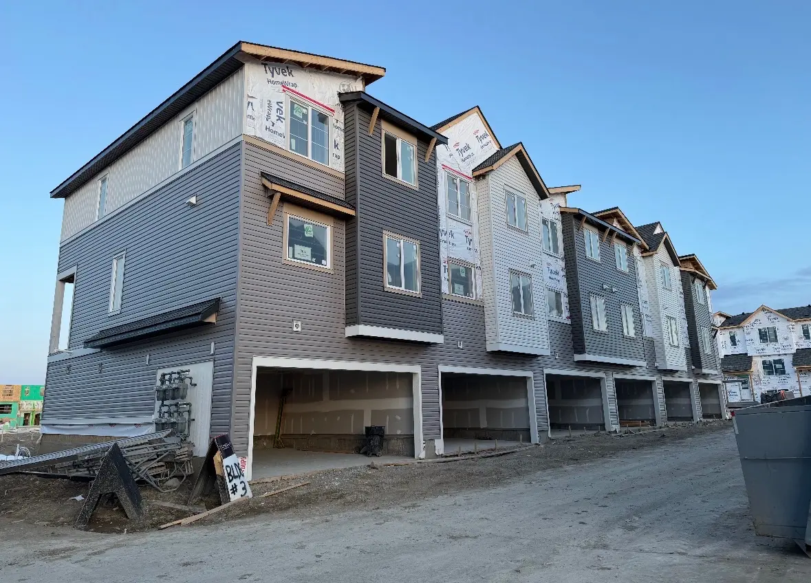 Row of three storey townhomes with grey siding, Tyvek house wrap and open garages