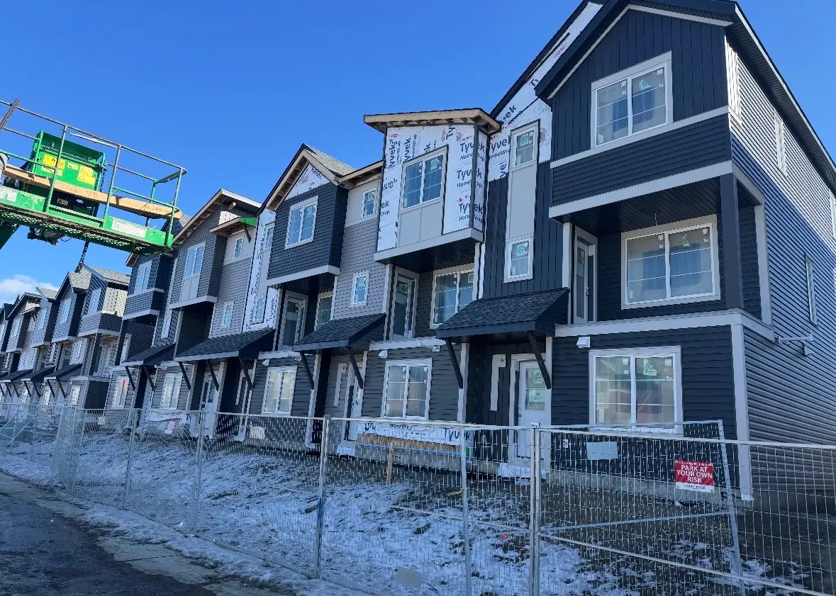 Row of dark siding townhomes with a boom lift and site fencing out front