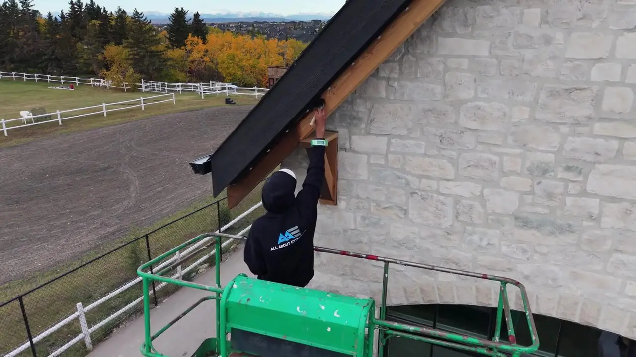 Video of an All About Exteriors painter on a lift painting the trim on a stone home