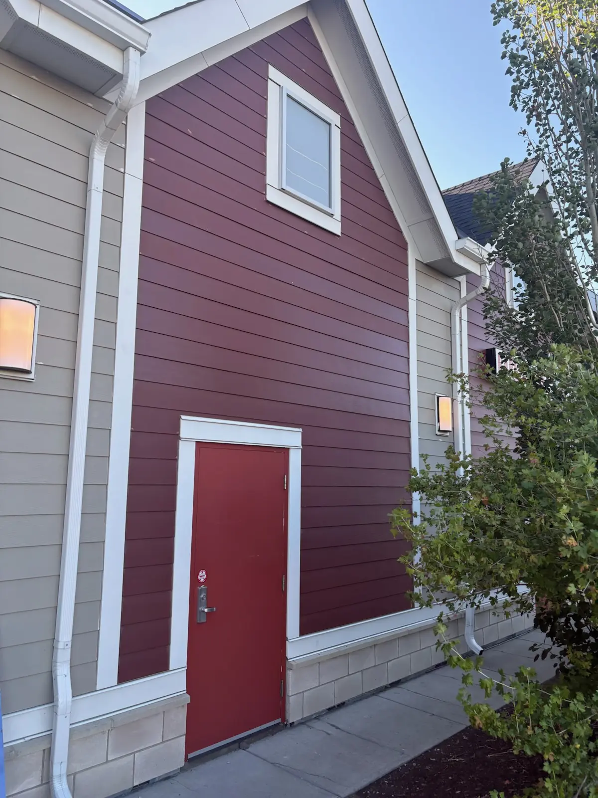 Red lap siding and a red entry door with white trim and downspouts on a townhome