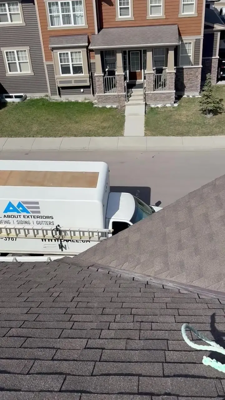 Video of an All About Exteriors roofer in a safety harness working on a shingle roof