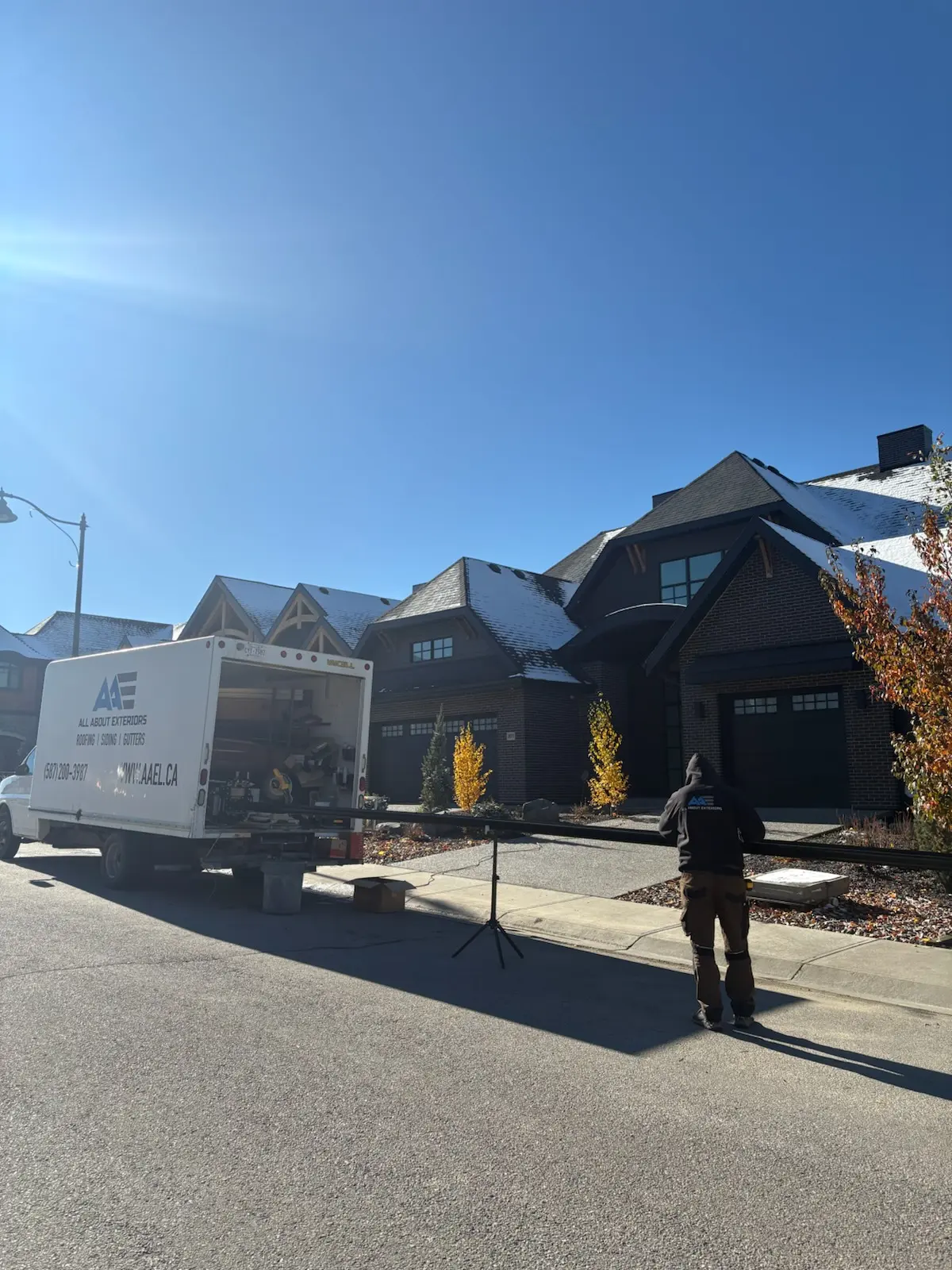 All About Exteriors box truck and crew member working on a gutter run in front of a dark brick home with a snowy roof
