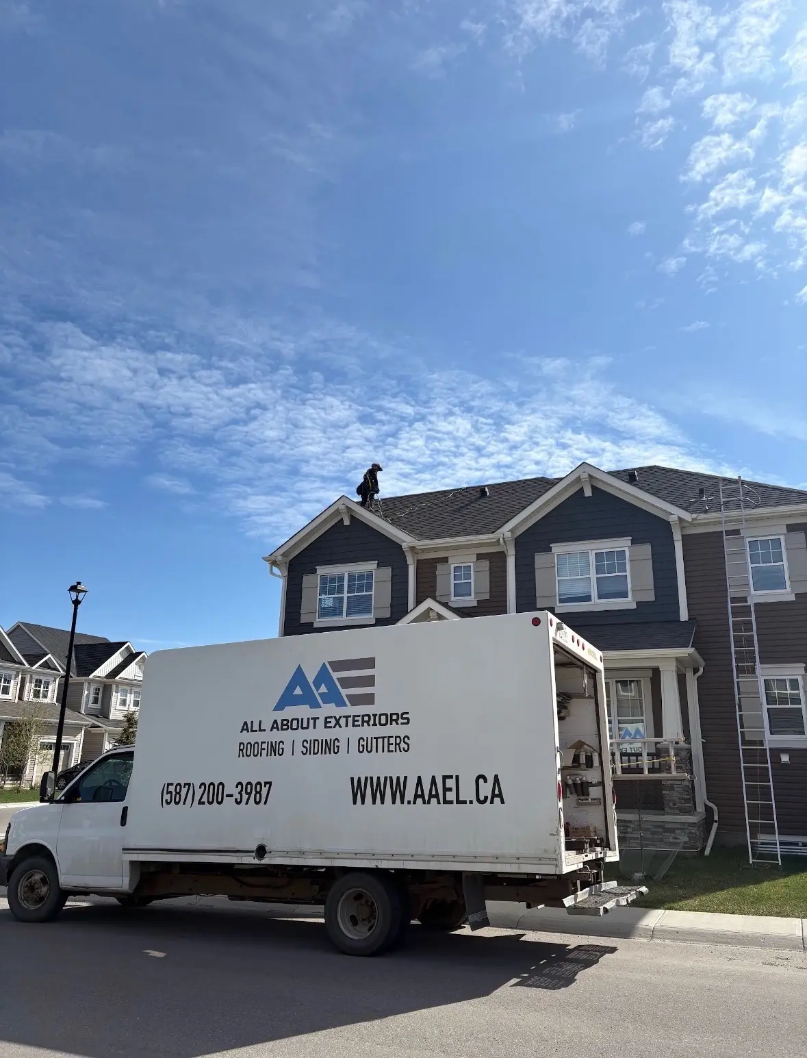 All About Exteriors box truck parked in front of a two storey home with a roofer working on the shingle roof