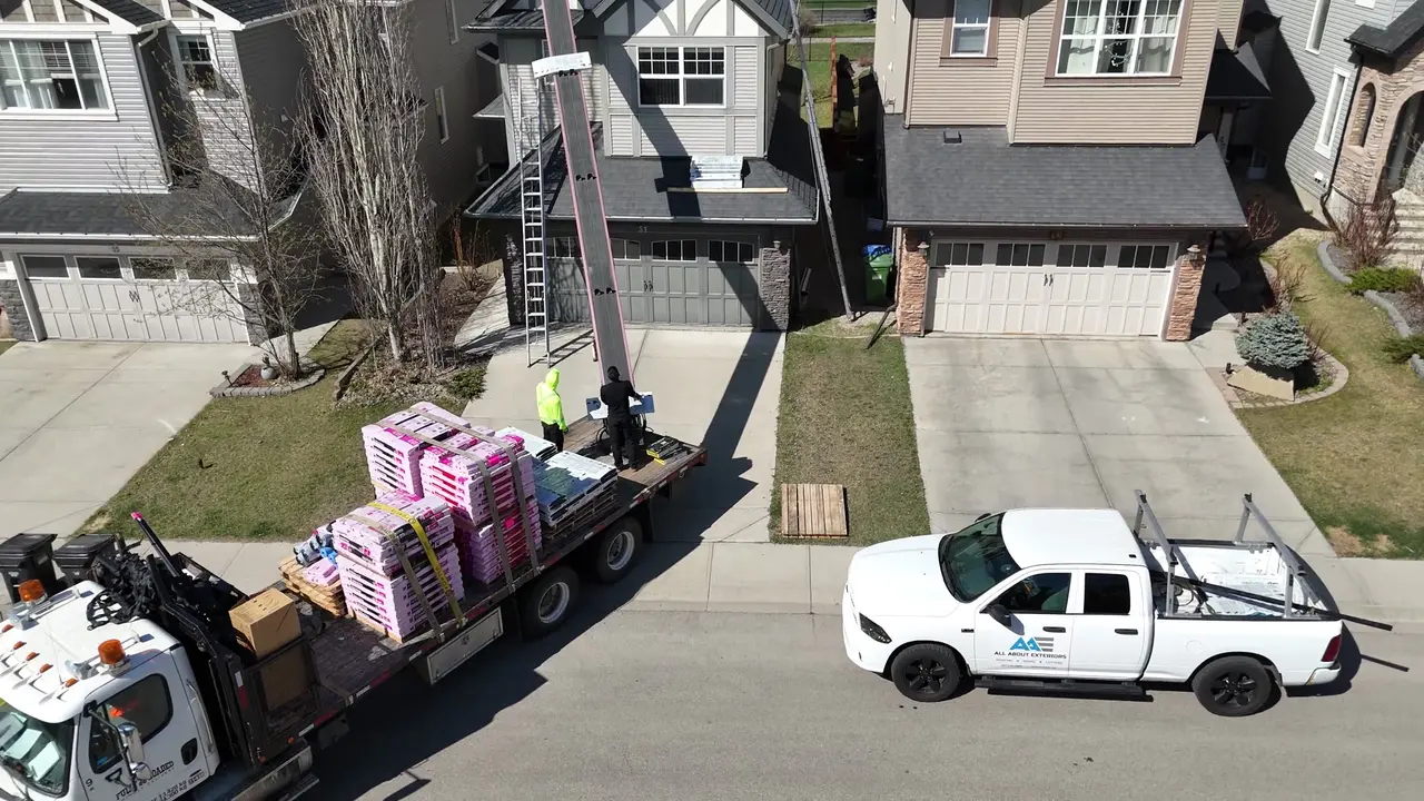 Drone video of a boom truck delivering shingle bundles to a roof while the crew works