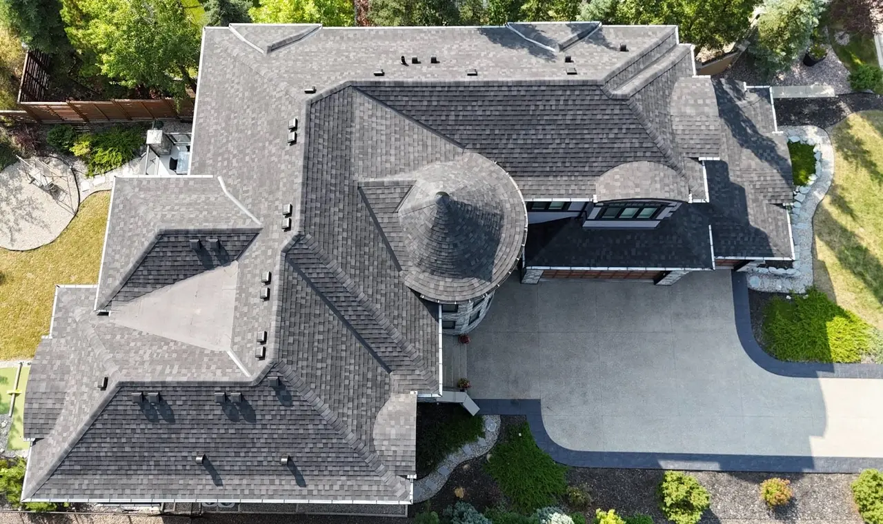 Aerial view of a new dark grey shingle roof with a round turret on a large home