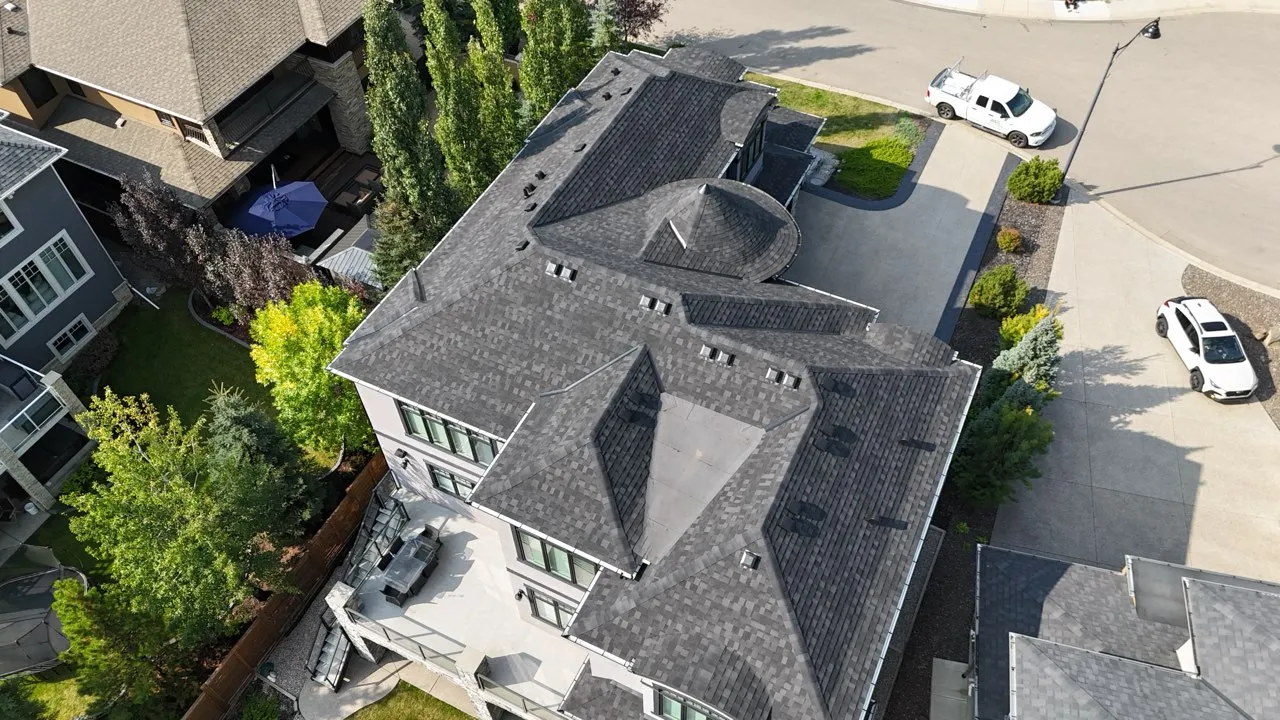 Aerial view of a new dark grey shingle roof on a large home with several hips and valleys