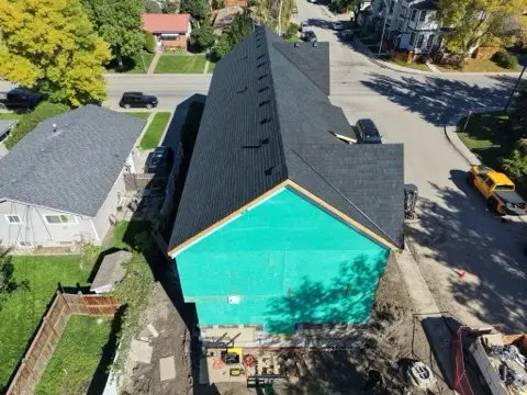 Aerial view of a new shingle roof on a home with teal house wrap on the end wall