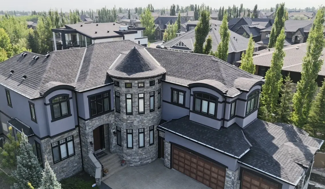 Aerial view of a large home with a natural stone turret and entry, stucco walls and a dark shingle roof