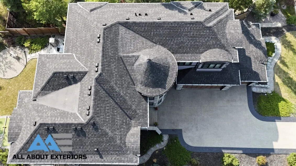 Drone view down onto the hip roof and stone turret of a large stucco and stone home