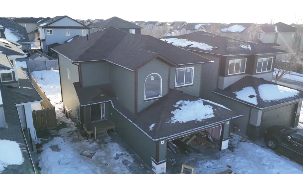 Drone view of a two storey home with a dark shingle roof and green siding in early winter snow